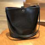 Brown leather bucket bag with shoulder strap and snap closure on wooden table