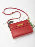 Red leather crossbody bag with gold buckle on a white surface over magazines