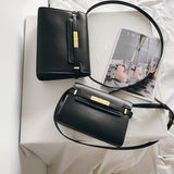 Minimalist black leather crossbody handbags with gold hardware on a white cloth, next to a magazine.