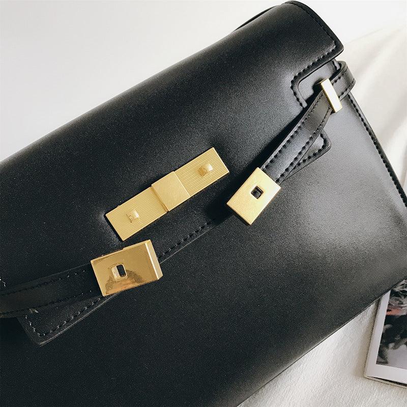 Black leather crossbody bag with gold hardware and minimalist design on white background