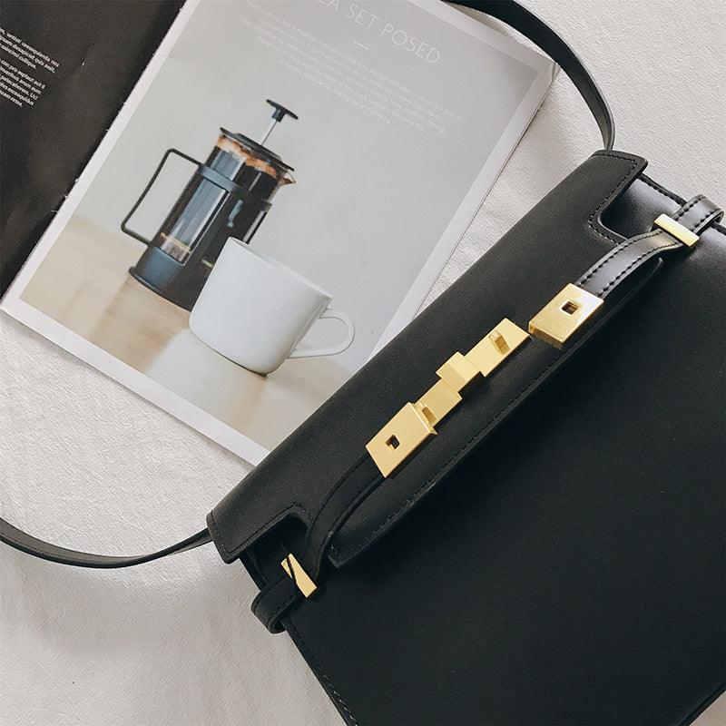 Black leather crossbody bag with gold hardware on a table beside a magazine and coffee cup