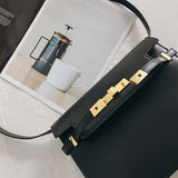 Black leather crossbody bag with gold hardware on a table beside a magazine and coffee cup
