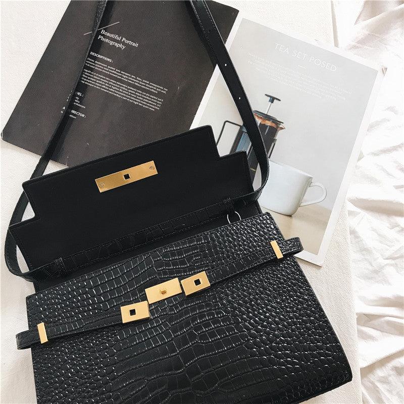 Black crocodile-embossed leather crossbody bag with gold hardware on a white surface