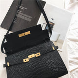 Black crocodile-embossed leather crossbody bag with gold hardware on a white surface