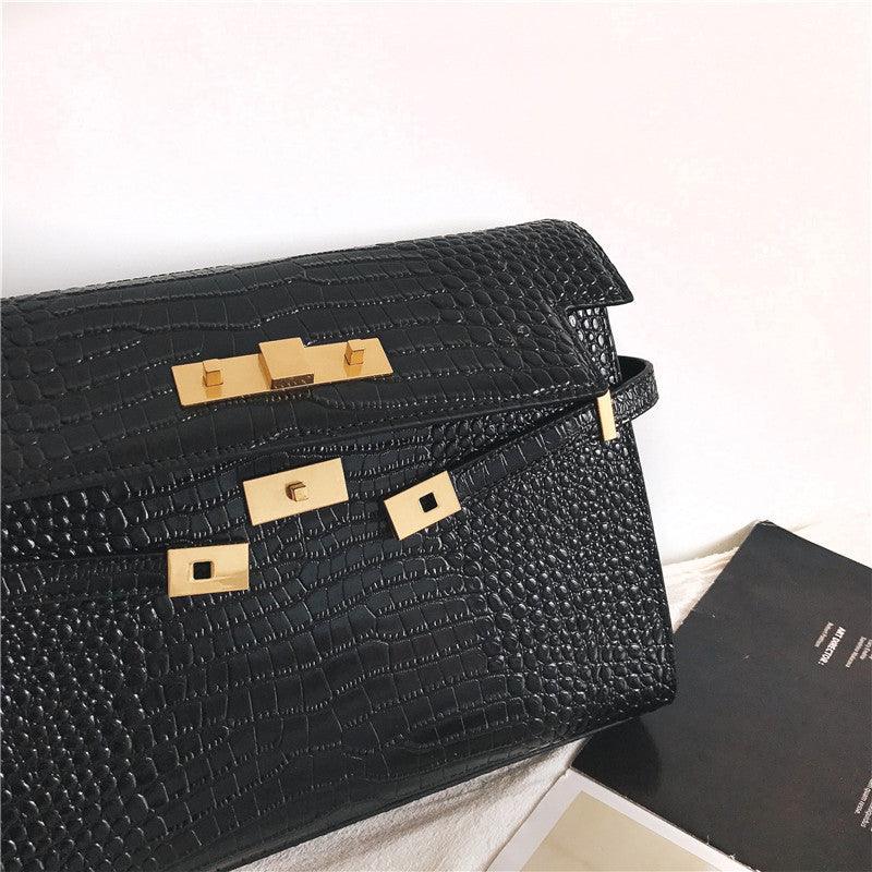 Black crocodile-embossed leather crossbody bag with gold hardware on a light background