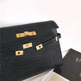 Black crocodile-embossed leather crossbody bag with gold hardware on a light background