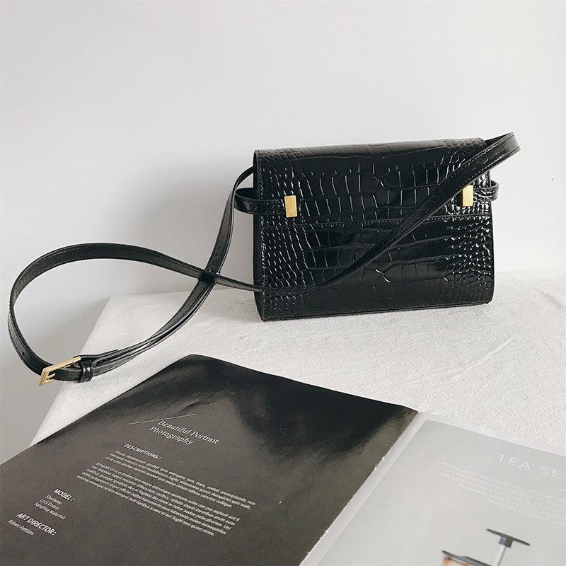 Black leather crossbody bag with crocodile texture and gold accents on a white surface
