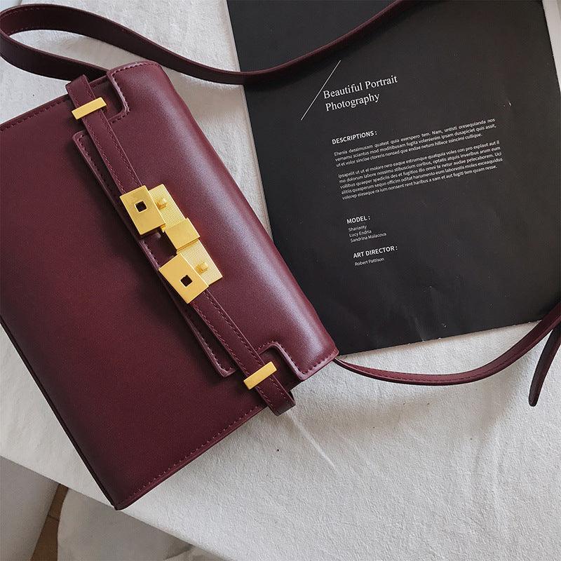 Burgundy leather crossbody bag with gold hardware on a white surface, minimal design