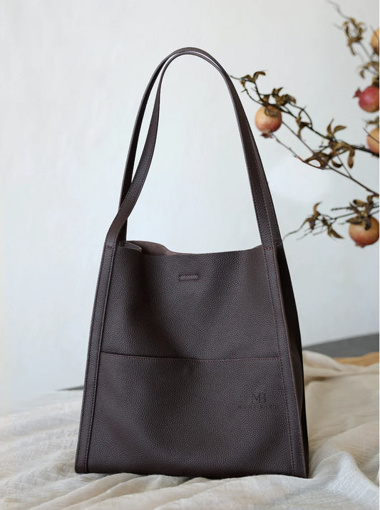Minimalist dark brown grain cowhide leather tote bag with shoulder straps on fabric.