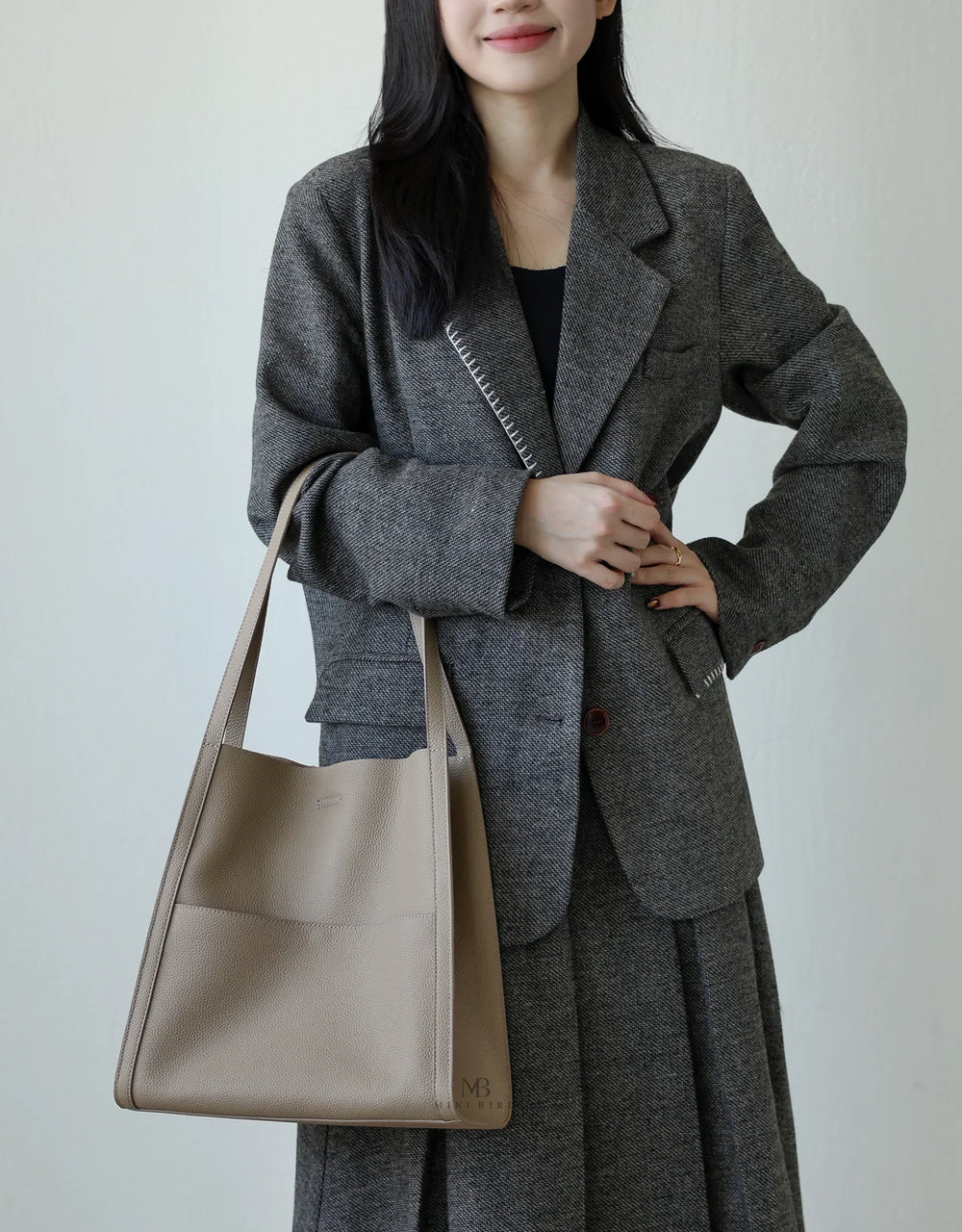 Woman in a grey blazer holding a beige grain cowhide leather tote bag with shoulder straps