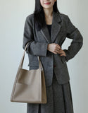 Woman in a grey blazer holding a beige grain cowhide leather tote bag with shoulder straps