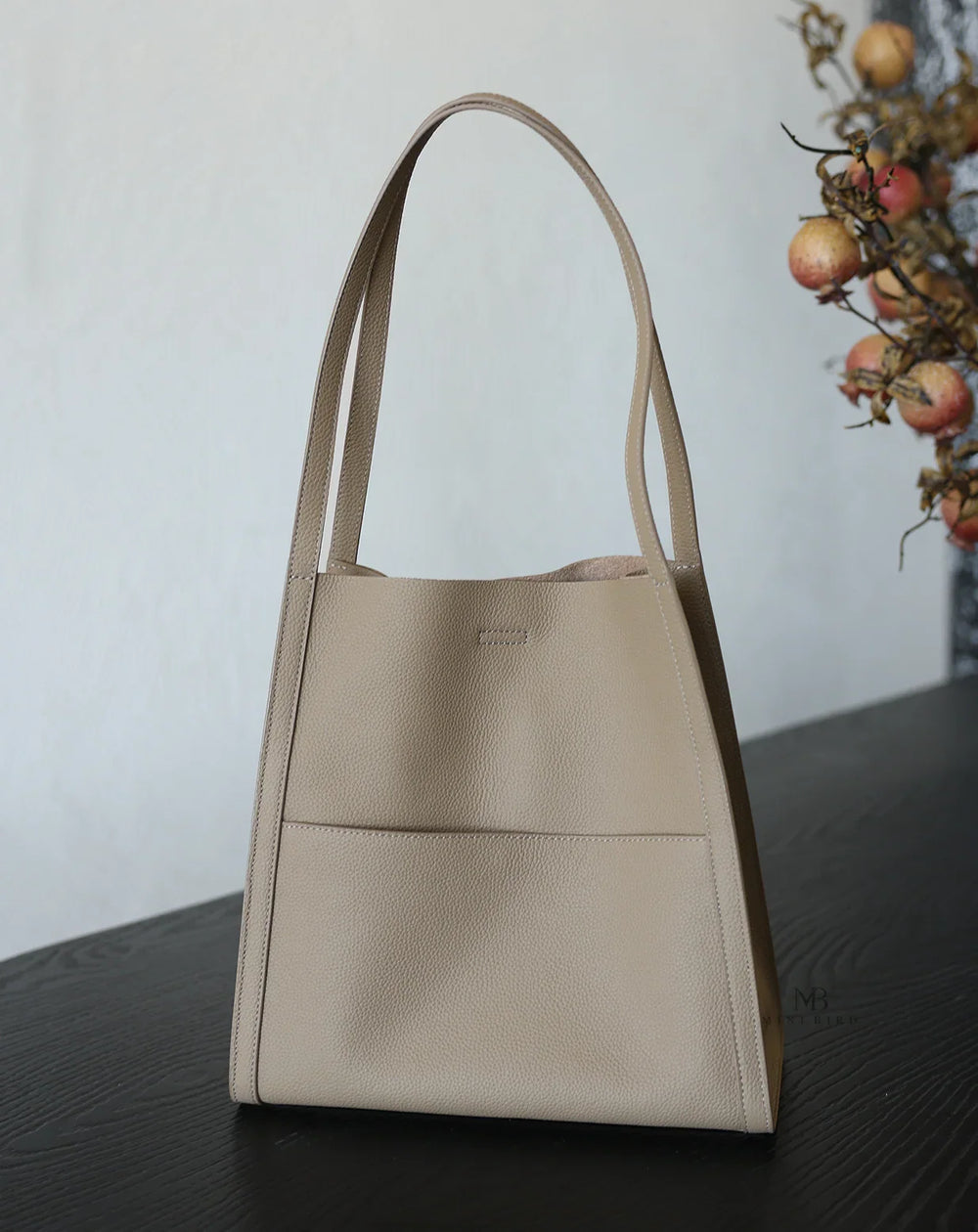 Beige grain cowhide leather tote bag with minimalist design on dark wooden table