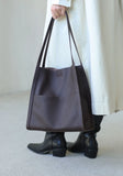 Woman holding large brown grain cowhide leather tote bag with long straps, wearing boots and a light coat.