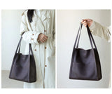Minimalist dark brown leather tote bag with shoulder straps, shown worn and hand-held