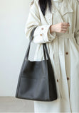Minimalist black grain cowhide leather tote bag with shoulder straps, styled on woman in beige coat