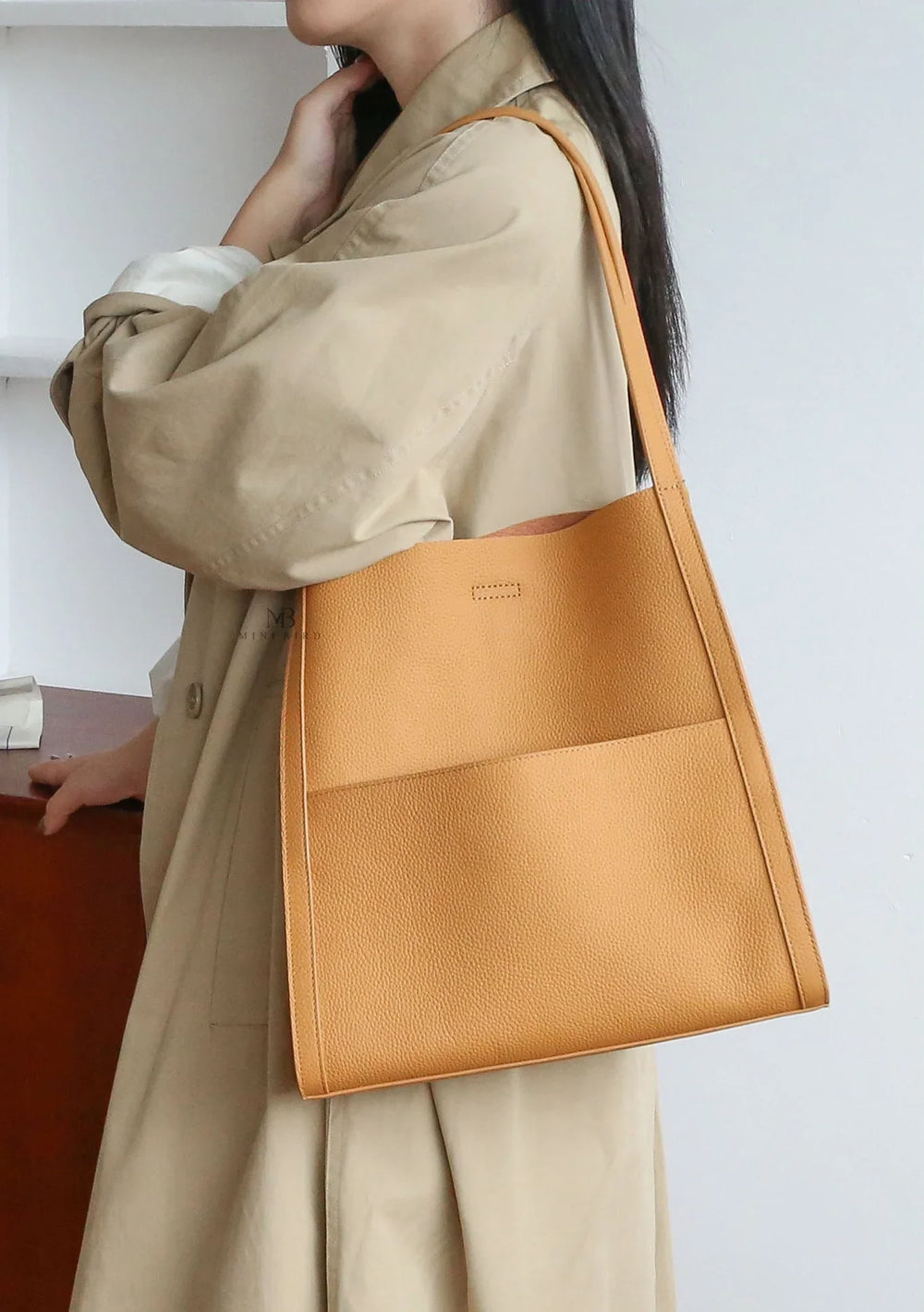 Minimalist tan leather tote bag with grain cowhide texture on woman's shoulder