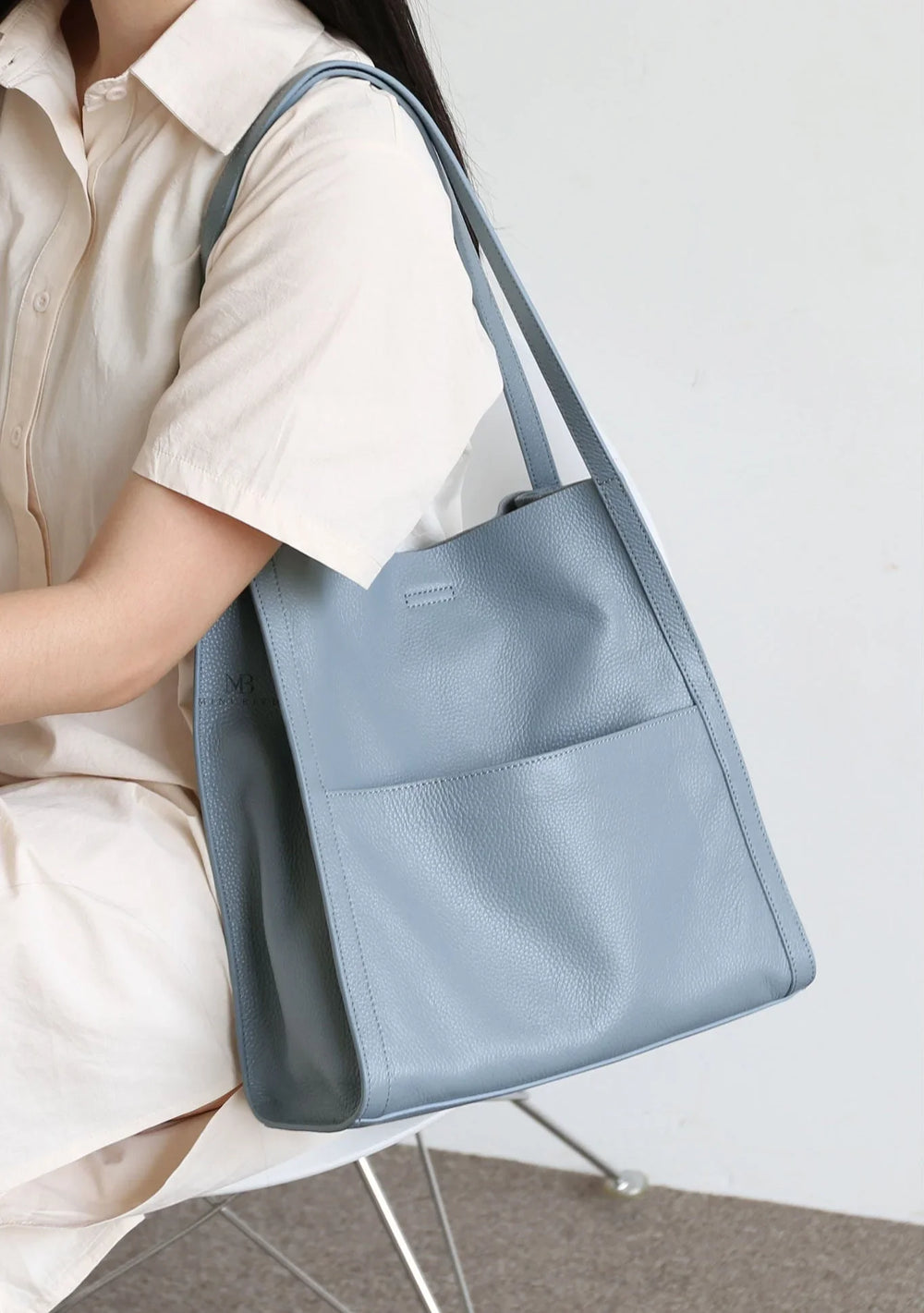 Woman holding a light blue grain cowhide leather tote bag with minimalist design
