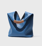 Minimalist blue genuine leather tote bag with tan woven handle on white background