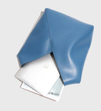 Minimalist blue leather tote bag with laptop and magazine inside on light background