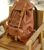Full grain brown cowhide leather backpack with buckles on a wooden chair