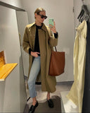 Woman in sunglasses and beige coat holding large brown leather bucket bag, casual fashion look