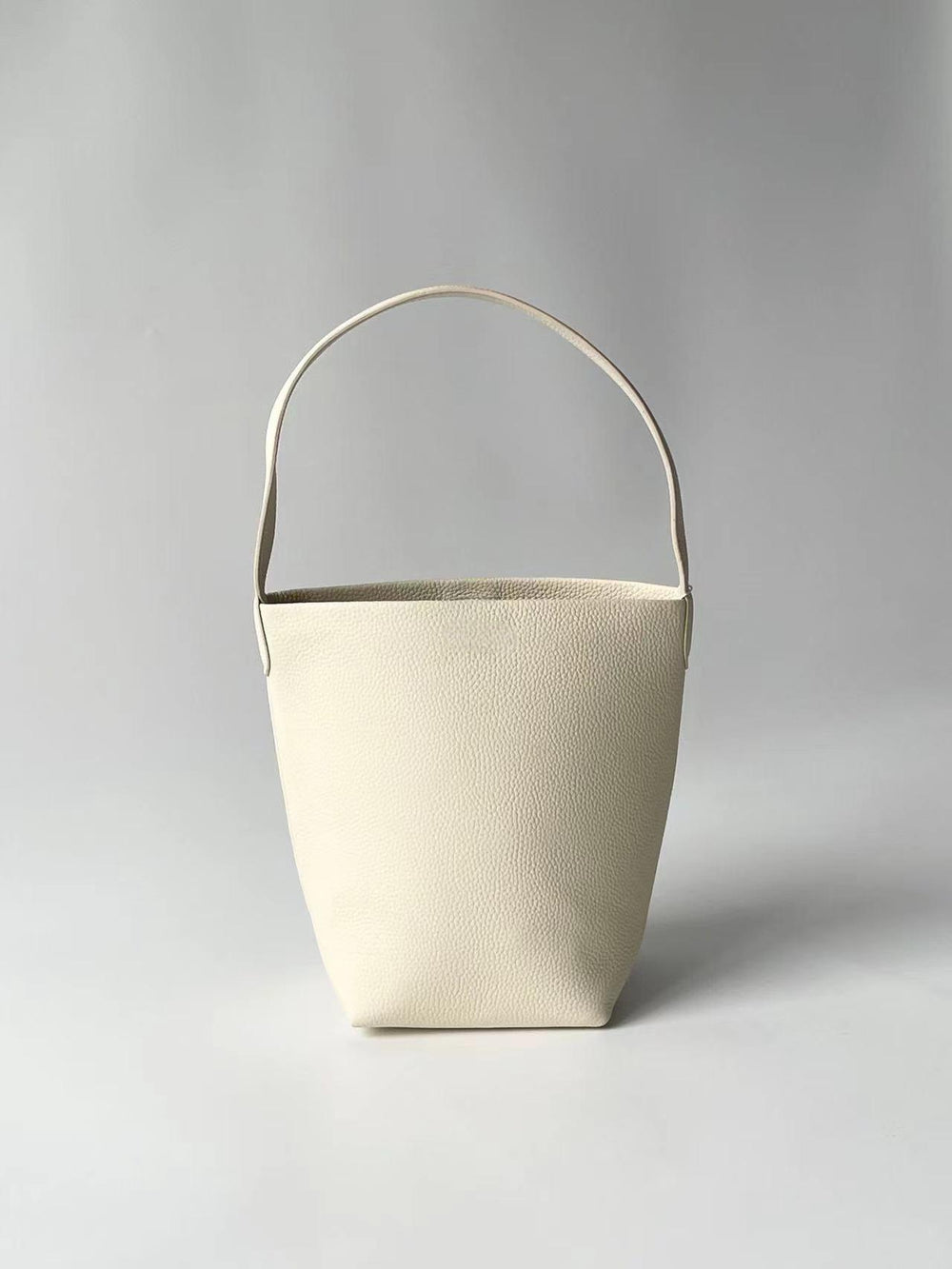 Minimalist large cream leather bucket bag with wide shoulder strap on neutral background