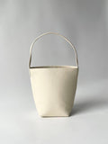 Minimalist large cream leather bucket bag with wide shoulder strap on neutral background