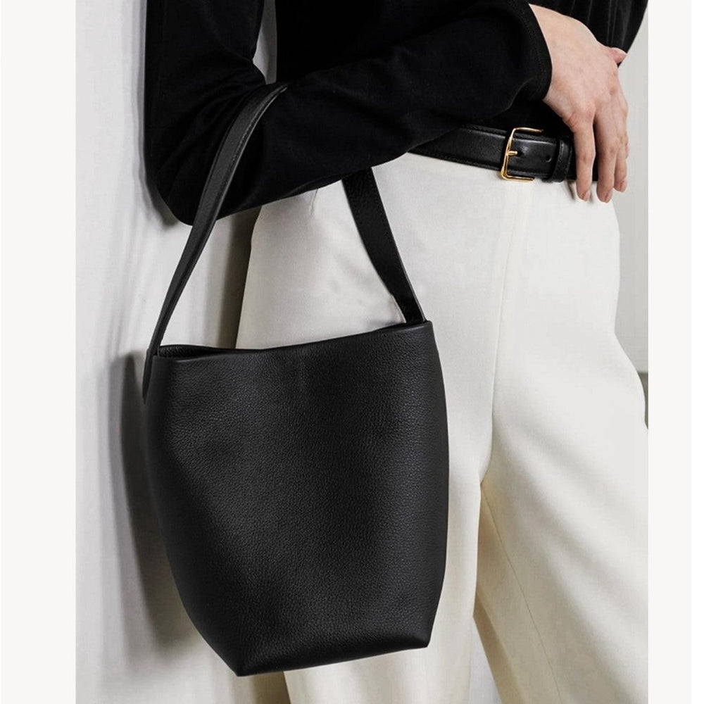Minimalist black leather bucket bag with shoulder strap, styled with white pants
