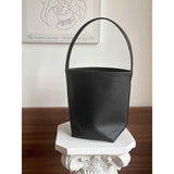 Minimalist black leather bucket bag with shoulder strap on a white pedestal indoors