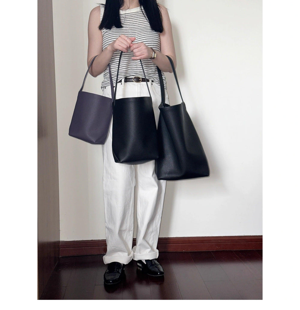 Woman in striped top holding three minimalist leather bucket bags in black and dark purple
