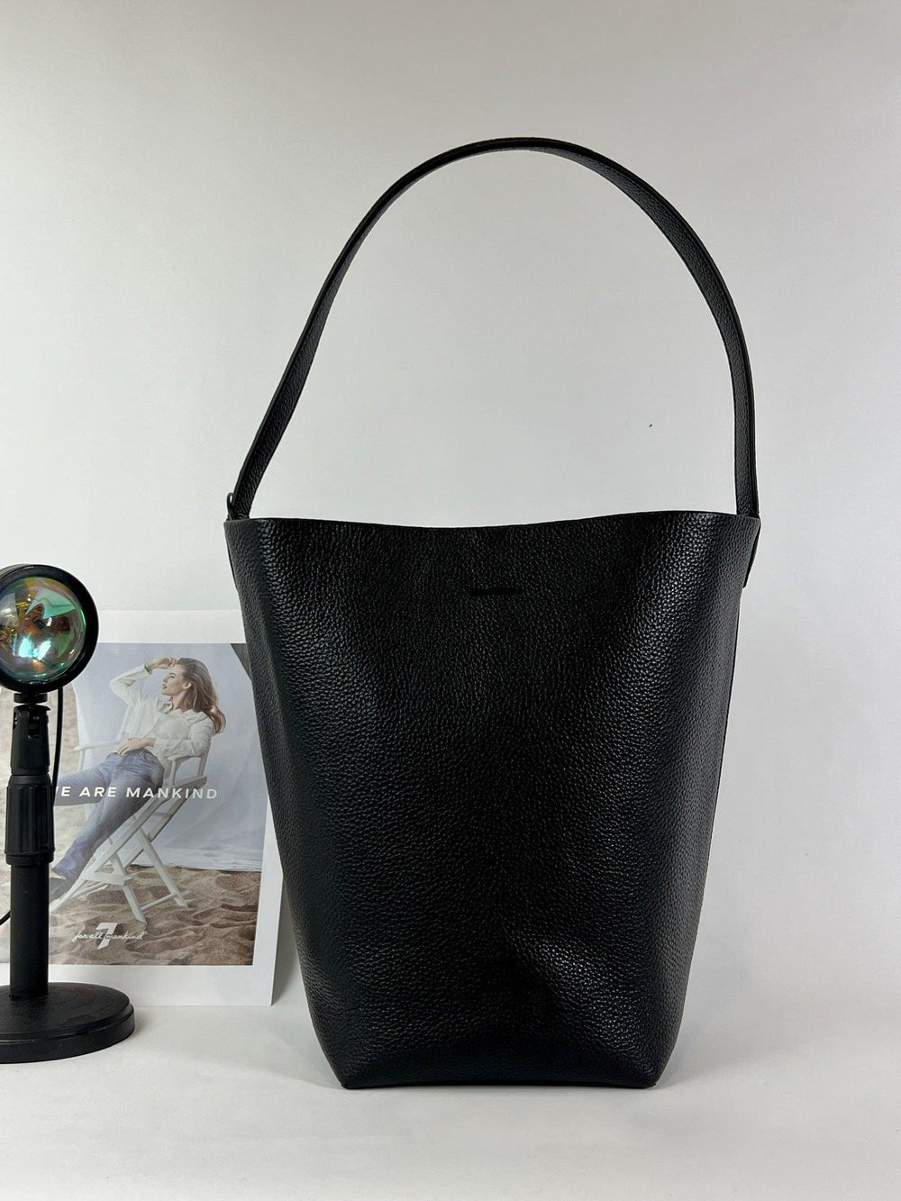 Minimalist black leather bucket bag with single shoulder strap on white background