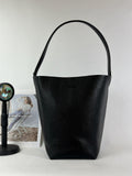 Minimalist black leather bucket bag with single shoulder strap on white background