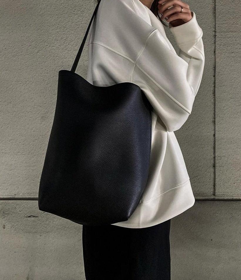 Minimalist black leather bucket bag tote with shoulder strap, styled with casual outfit