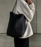 Minimalist black leather bucket bag tote with shoulder strap, styled with casual outfit