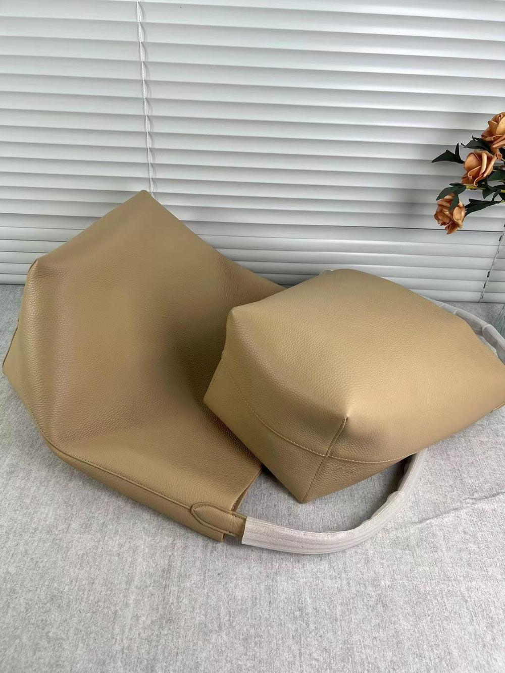 Minimalist tan leather bucket bag with wide handle on grey surface, modern style tote