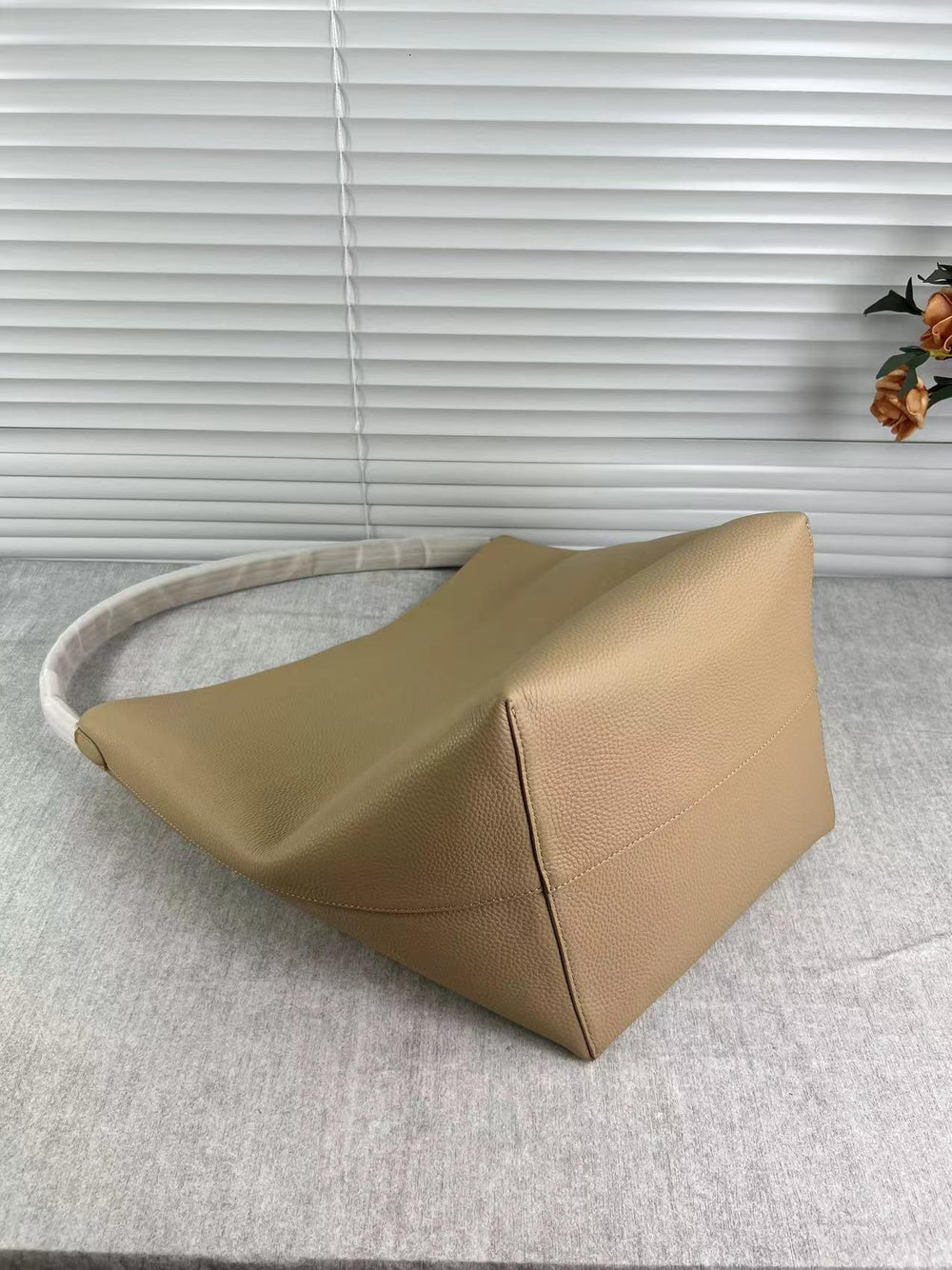 Minimalist tan leather bucket bag with shoulder strap on a grey surface, home setting