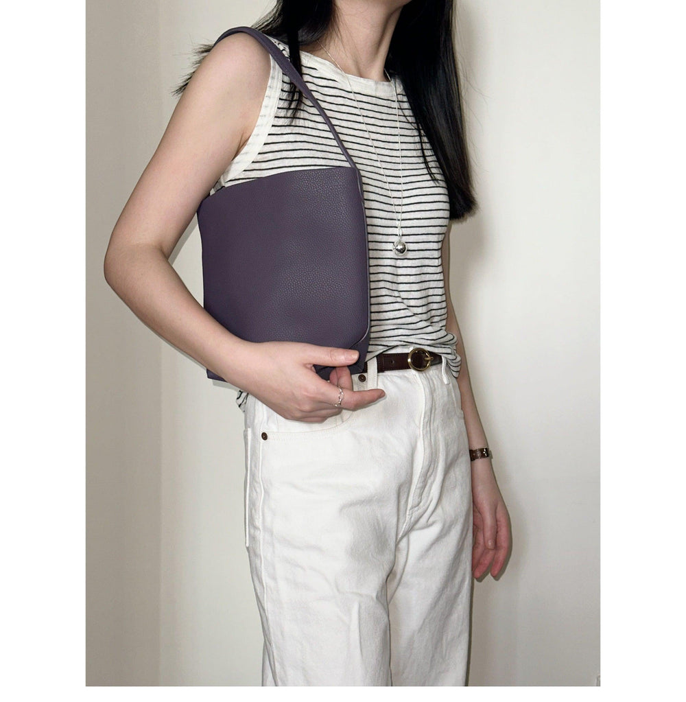 Woman wearing striped top and white pants holding minimalist leather bucket shoulder bag