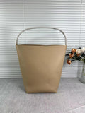 Minimalist tan leather bucket bag with sturdy handle on a grey surface, flowers in background