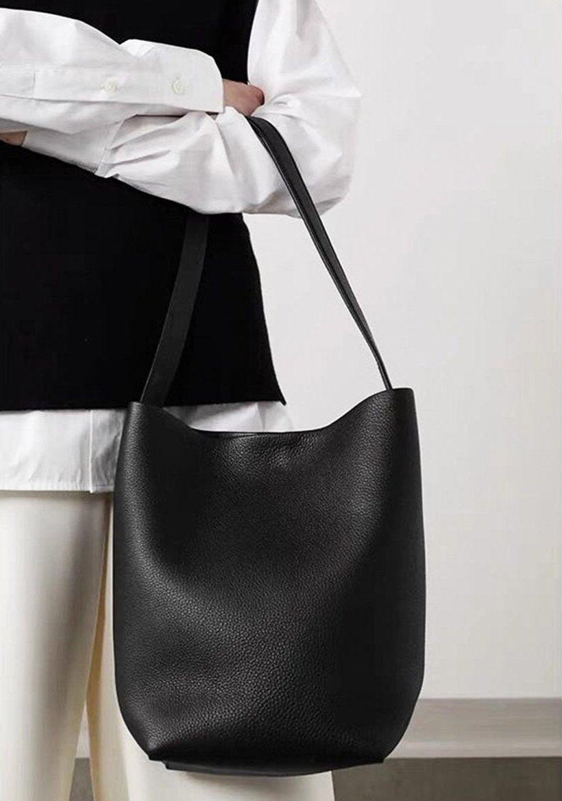 Minimalist black leather bucket bag with shoulder strap, worn by person in white shirt