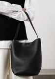 Minimalist black leather bucket bag with shoulder strap, worn by person in white shirt