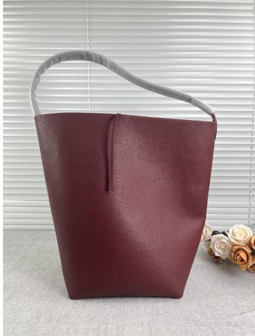 Minimalist burgundy leather bucket bag with single shoulder strap on neutral background