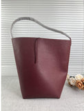 Minimalist burgundy leather bucket bag with single shoulder strap on neutral background