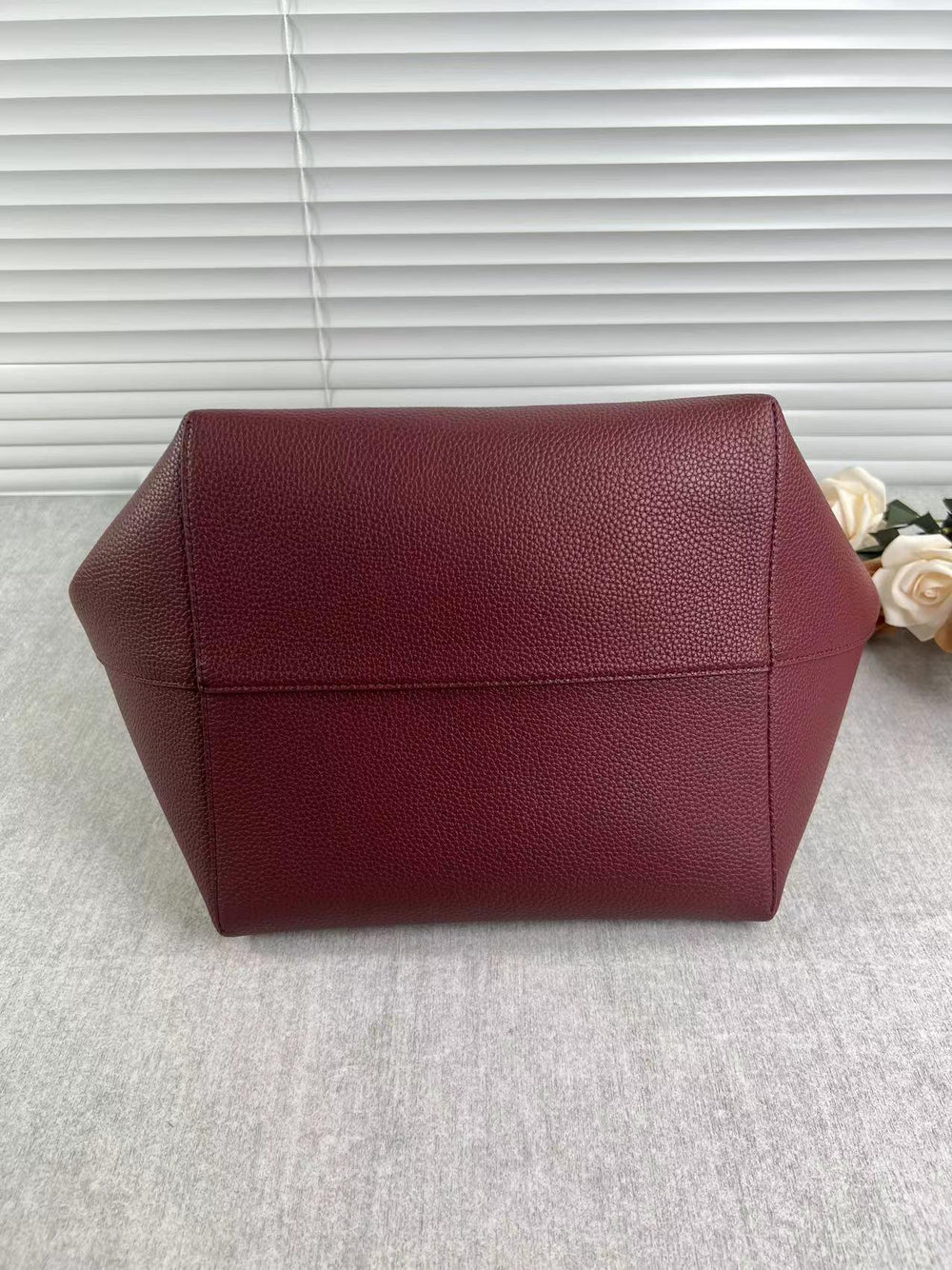 Large burgundy leather bucket bag with textured finish on a neutral surface, minimalist style
