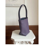 Minimalist purple leather bucket bag with shoulder strap on decorative white pedestal