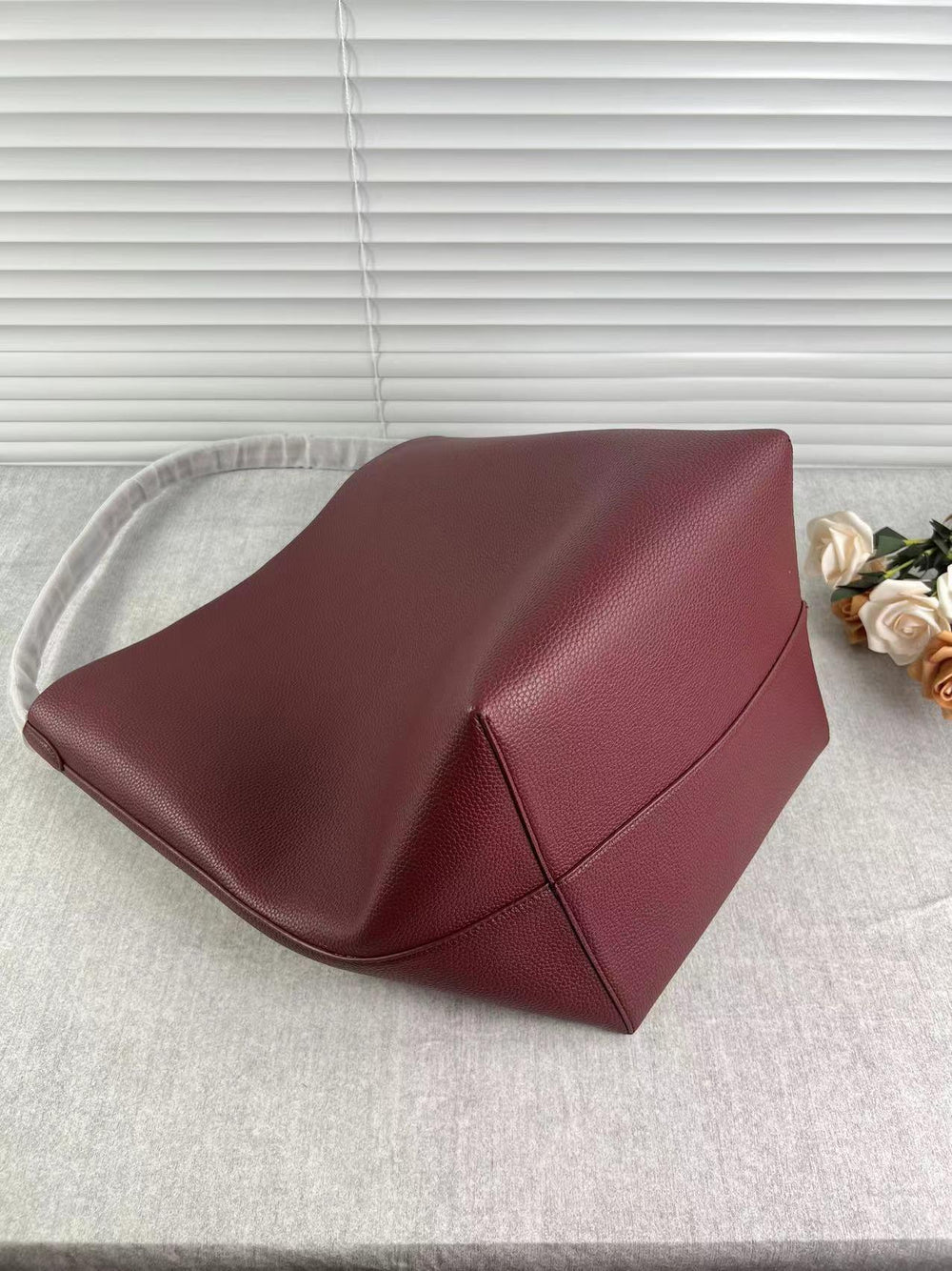 Minimalist large maroon leather bucket bag with shoulder strap on light fabric surface