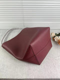 Minimalist large maroon leather bucket bag with shoulder strap on light fabric surface