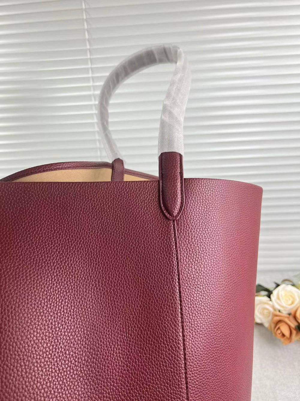 Close-up of a large tan pebbled leather bucket bag with shoulder strap, minimalist style