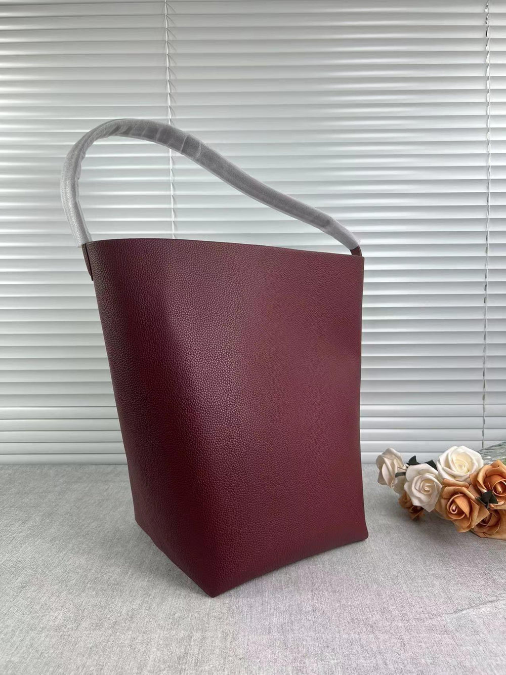 Minimalist large tan leather bucket bag with shoulder strap on neutral background
