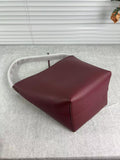 Minimalist burgundy leather bucket bag with shoulder strap on a light fabric surface