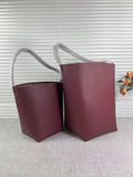 Two large minimalist tan leather bucket bags with shoulder handles on a neutral background.